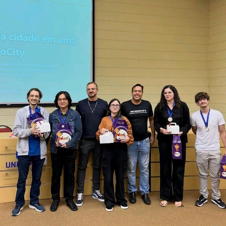 Grupo com medalhas e troféus em evento acadêmico.